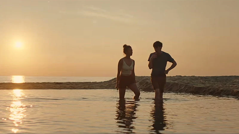 Two characters standing in a lake beneath a golden sunset in An Autumn Summer.